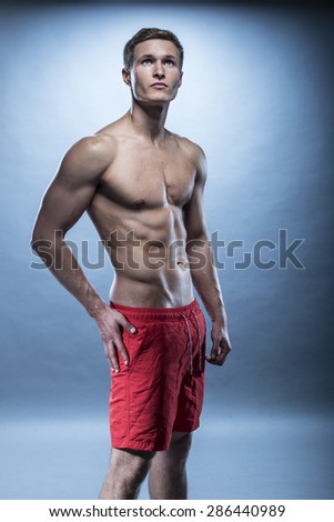 blonde Male fitness model wearing red shorts on blue