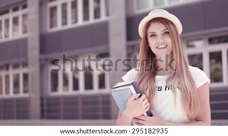 Half Body Shot of a Pretty Blond Young Student Holding Books, Smiling at the Camera Against the University.