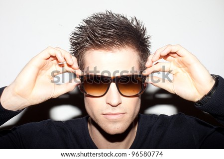 Trendy young man with spiky hair with his hands raised to a pair of sunglasses.