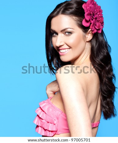 Stunning young woman with long dark hair wearing a bikini and tropical flower in her hairs smiles enchantingly at the camera with copyspace