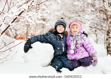 happy brother and sister are smiling and hugging in the snowfall. two children playing in the snow