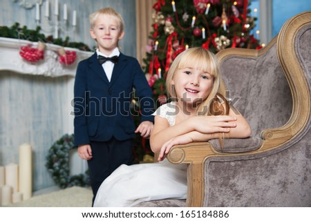 Happy sister sitting in a armchair and brother standing near. little friends enjoying New Year party, Christmastime holidays, best friends, happiness concept