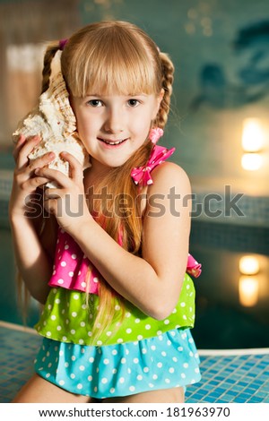 portrait of little girl with sea shell in her hands in the swimming pool in sport club