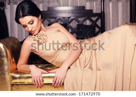 beautiful girl with black hair in beige silk dress lying on sofa