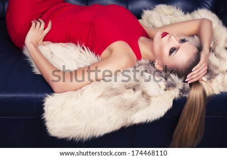 sexy woman with blond hair in red dress lying on the fur coat
