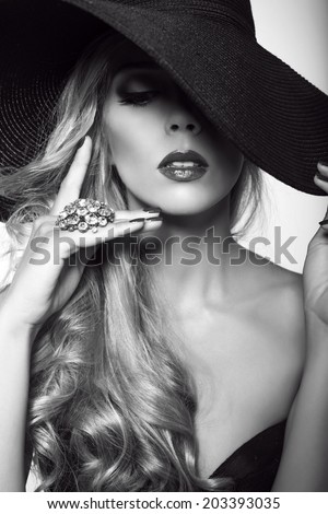 black and white fashion portrait of beautiful glamour woman with long blond hair in elegant black hat with  big ring