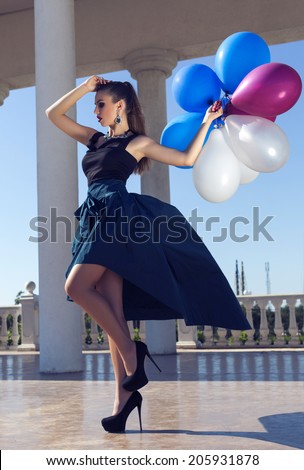 fashion photo of beautiful glamour young woman in elegant dress and bijou holding white and blue balloons