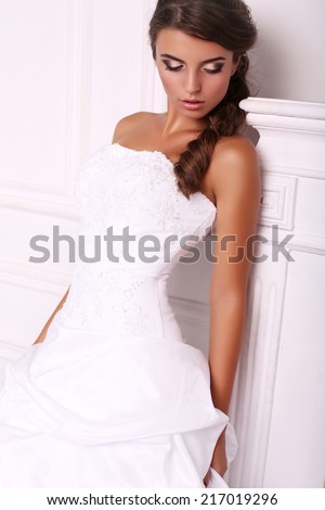 fashion photo of beautiful elegant bride with dark hair in wedding dress posing at studio