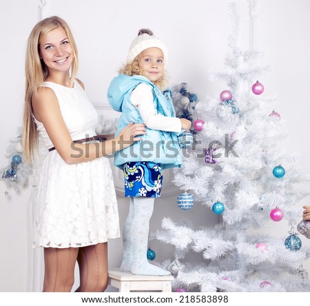 cute photo of little girl with blond curly hair and her pregnant mother decorating Christmas tree