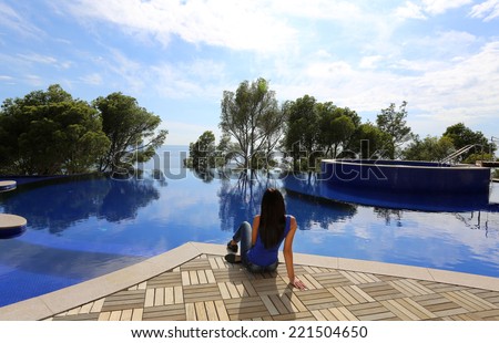 fashion outdoor photo of beautiful woman with dark hair relaxing beside a grand swimming pool