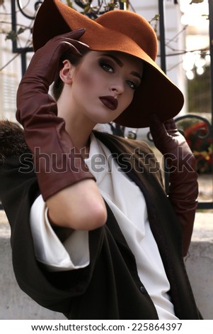 fashion outdoor photo of beautiful young woman with bright makeup wearing elegant coat with fur,felt hat and leather gloves