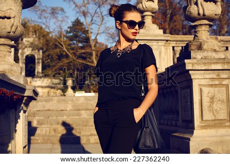 fashion outdoor photo of beautiful young woman with dark hair in elegant clothes and sunglasses posing in sunny autumn park