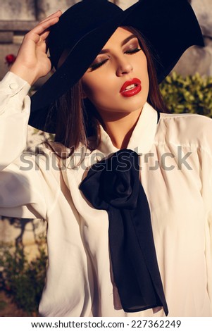fashion outdoor photo of beautiful ladylike woman with dark hair wearing elegant blouse and black hat,posing in autumn park