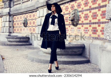 fashion outdoor photo of beautiful ladylike woman with dark hair wearing elegant coat and felt hat and posing in autumn park