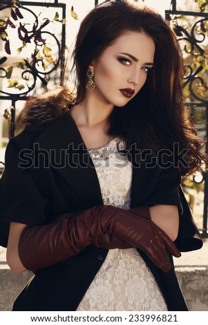fashion outdoor photo of beautiful ladylike woman with dark hair wearing elegant coat with fur and leather gloves