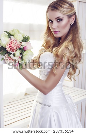 fashion interior photo of beautiful bride with blond hair in elegant wedding dress,holding a bouquet of flowers