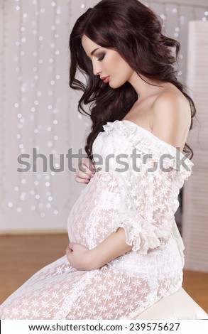 fashion interior photo of beautiful pregnant woman with long dark hair wearing lace dress