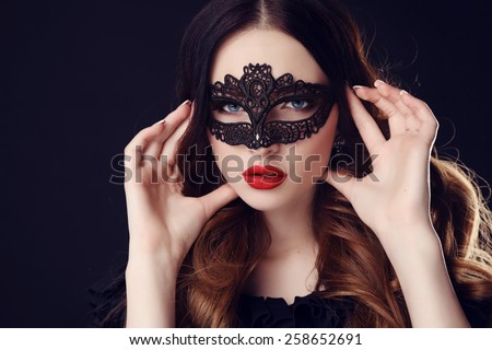 fashion photo of gorgeous woman with dark hair and blue eyes, with lace mask on her face,posing in dark studio