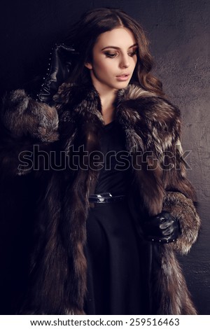 fashion photo of sexy woman with dark hair in luxurious fur coat and black leather gloves posing in studio