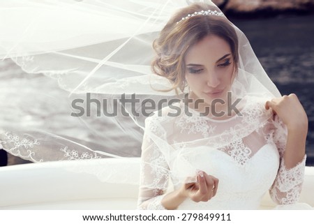 fashion photo of beautiful sensual bride with dark hair in luxurious lace wedding dress posing on yacht