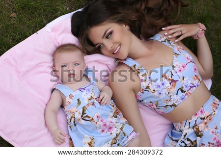 fashion outdoor photo of beautiful family look.beautiful mother with long dark hair posing with her little cute baby in similar dresses with flowers print
