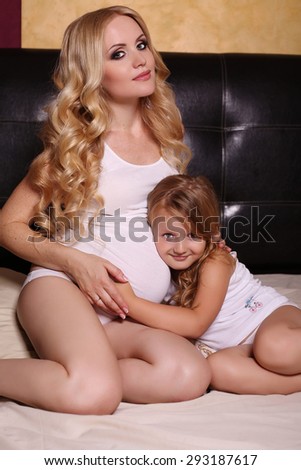 interior photo of beautiful family. pregnant mother with luxurious blond hair having fun with her little cute daughter