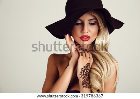 fashion studio portrait of beautiful sensual woman with blond hair with evening makeup and henna tattoo on hands