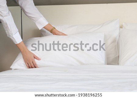 Room service maid cleaning and making bed hotel room concept, female hands of chambermaid holding  pillow for making bed in hotel room.