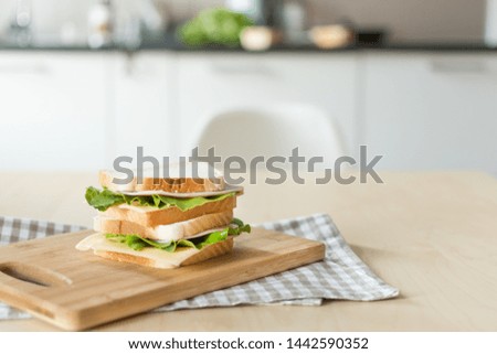 Sandwich with cheese and ham on cutting board on the table in the bright kitchen. Lunch. Sandwich with lettuce. Healthy eating concept.