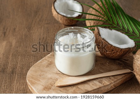 Jar of coconut butter and fresh coconuts with palm leaf on wooden background. Healthy vegan food.