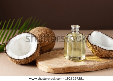 Bottle of coconut oil and fresh coconuts with palm leaf on wooden board over brown background. Coconut natural cosmetics.