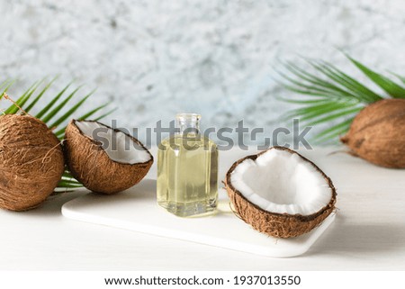 Bottle of coconut oil and fresh coconuts with palm leaf on white wooden table. Coconut natural cosmetics.
