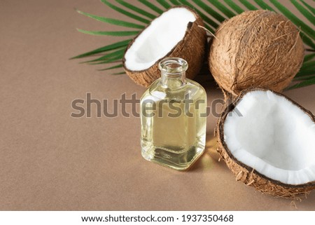 Bottle of coconut oil and fresh coconuts with palm leaf on brown background. Coconut natural cosmetics.