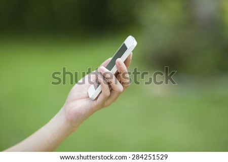 Closeup woman hand using smart phone against nature background