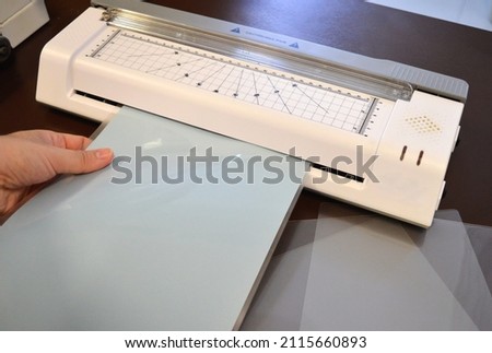 Worker laminating pouches with a light blue sheet inside on an office table, and some clear pouches on the right side. Foto d'archivio © 