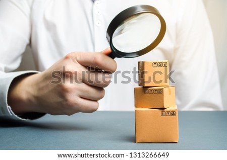 A man holds a magnifying glass above the boxes. Examination of goods for the presence of contraband, prohibited goods, defects. Quality control, authentication. study of consumer sentiment 商業照片 © 