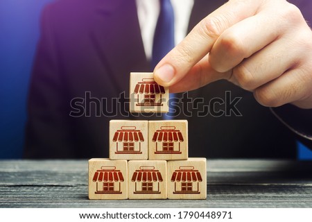 A man builds a pyramid from blocks of business shops. Building a successful business empire. Expansion and competitive growth. Franchise concession concept. Commercial network development. Foto d'archivio © 