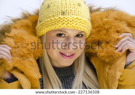 Young Caucasian girl in winter clothes, wearing yellow winter cap and jacket with fur