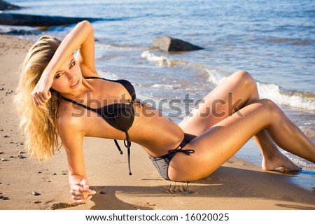 Young beautiful sexy blonde bikini model, laying on sea beach