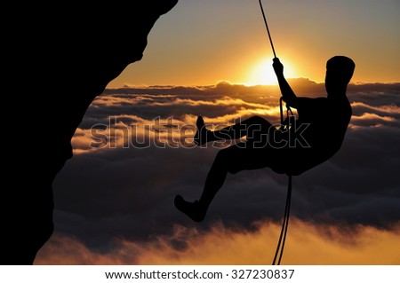 Climber silhouette high above clouds and mountains. Young man abseiling down during sunset.