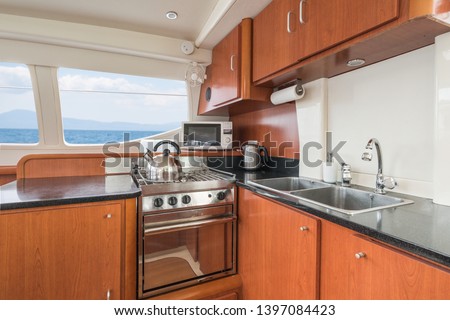 Clean and modern galley/kitchen of a private sailing catamaran with wooden cupboards, sink, oven, microwave and kettle, with Mediterranean sea view from the windows.  ストックフォト © 