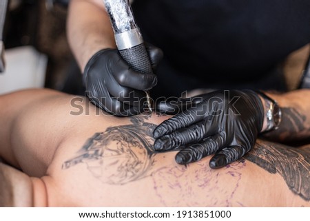 professional tattoo artist introduces black ink into the skin using a needle from a tattoo machine. tattoo art on body. Professional tattooist working black and white tattooing in studio.