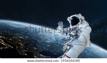 Space man astronaut greets and waves his hand in space on a background of the blue planet Earth. Space mission wallpaper, concept. Welcome to space