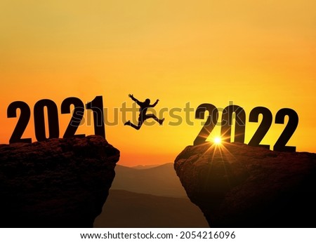 Man jumping on cliff 2022 over the precipice at amazing sunset. New Year's concept. Symbol of starting and welcome happy new year 2022. People enters the year 2022, creative idea