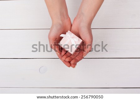 Female hand holding pink gift in hands on a white wooden table. View from the top.