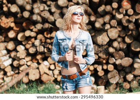 Portrait of a beautiful woman in sunglasses in denim shorts and jeans jacket on the sawmill.