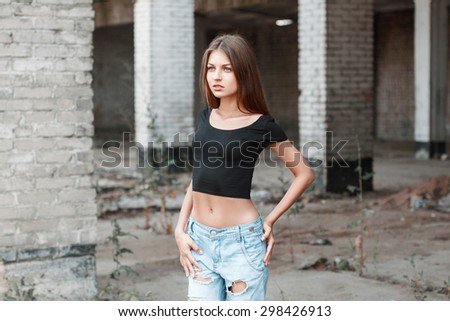 Beautiful girl in a black T-shirt and torn jeans near the brick columns.