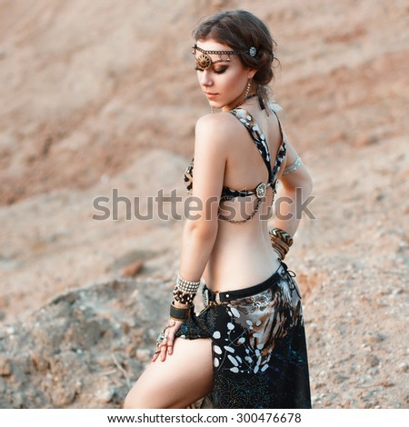 Pretty woman in an Indian tribal jewelry on a background of sand. Tribal fusion dance style.