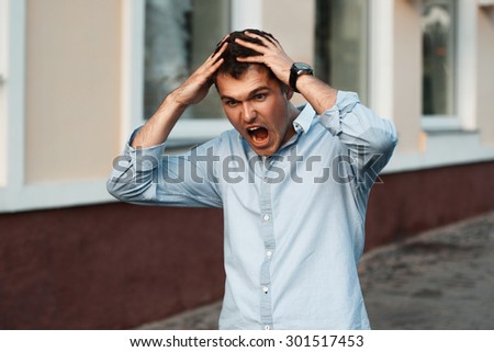 Portrait of young angry man with hands on head. Clings to his head and shouts
