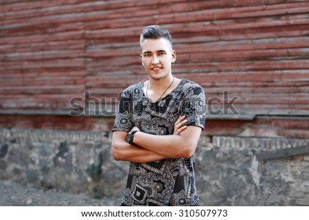 Young funny guy with a smile stands on the background of a wooden old house.